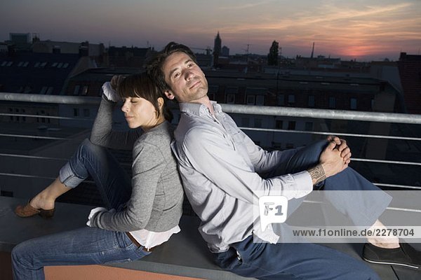 Ein Paar  das nachts Rücken an Rücken auf einer Dachterrasse sitzt.