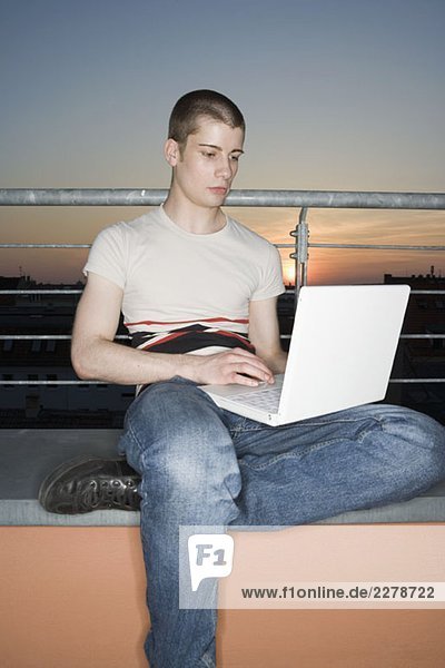 Ein junger erwachsener Mann  der einen Laptop auf einer Dachterrasse benutzt.