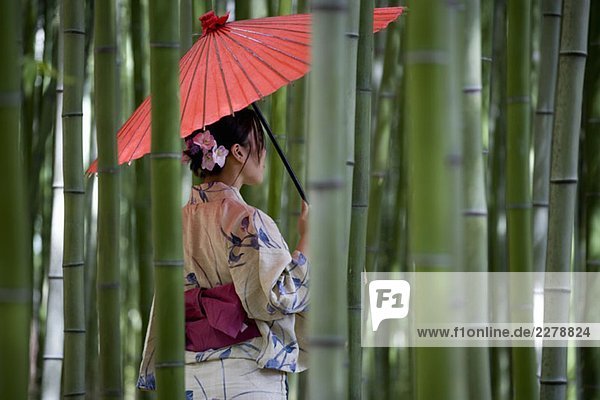 Eine Frau  die einen Kimono trägt und in einem Bambushain steht.