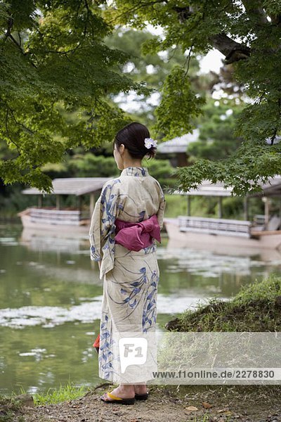 Eine Frau mit Kimono  die am Ufer eines Sees steht.