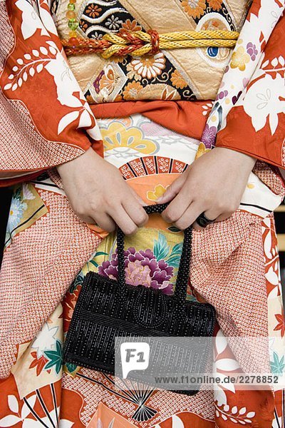 Mittelteil einer Frau  die einen Kimono trägt und eine Handtasche hält.
