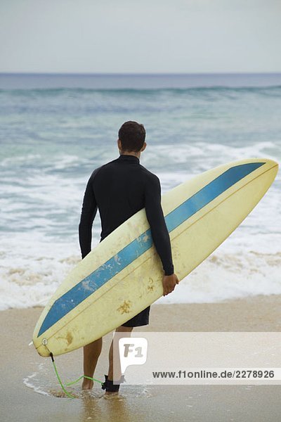 Ein Surfer  der sein Surfbrett hält.