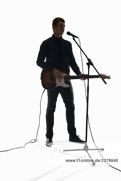 Studio shot of a man singing into a microphone and playing an electric guitar