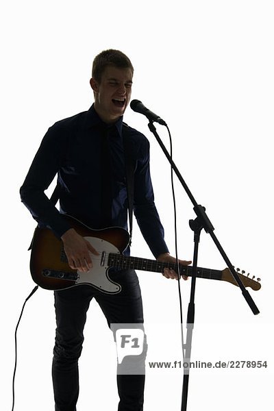 Studio shot of a man singing into a microphone and playing an electric guitar