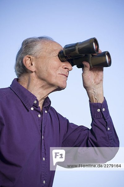 Ein älterer Mann  der ein Fernglas benutzt.