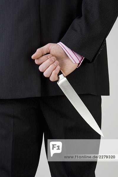 Ein Geschäftsmann  der das Messer hinter seinem Rücken hält.