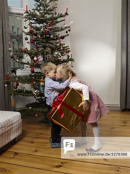 Bruder und Schwester küssen sich vor einem Weihnachtsbaum