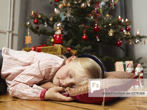 Ein Mädchen  das neben einem Weihnachtsbaum schläft.