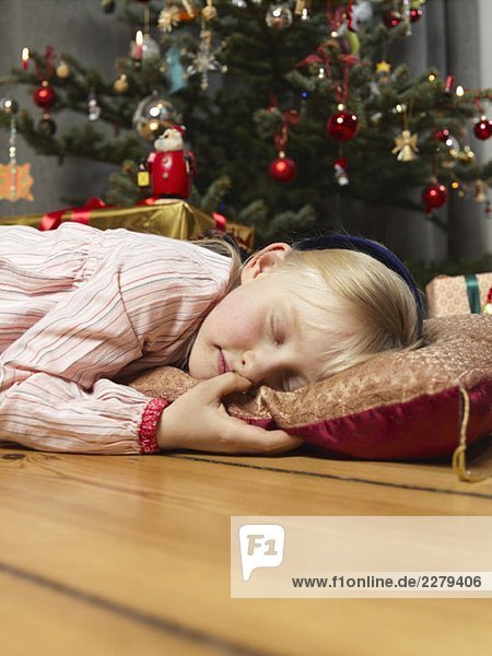 A girl sleeping next to a Christmas tree