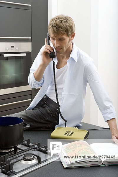 A man sitting on a kitchen worktop and using the telephone