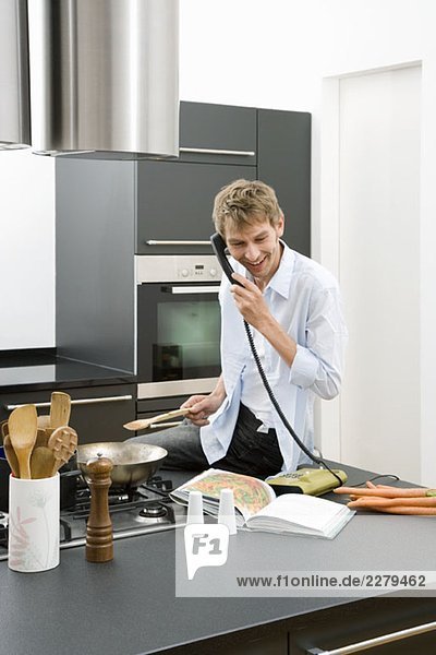 Ein Mann  der auf einer Küchenarbeitsplatte sitzt und das Telefon benutzt.