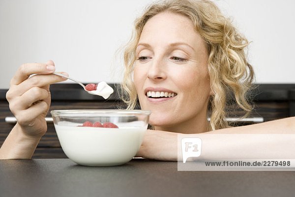 Eine Frau hält einen Löffel Joghurt und Himbeeren an den Mund.