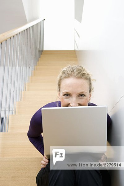 Eine erwachsene Frau  die mit einem Laptop auf einer Treppe sitzt.