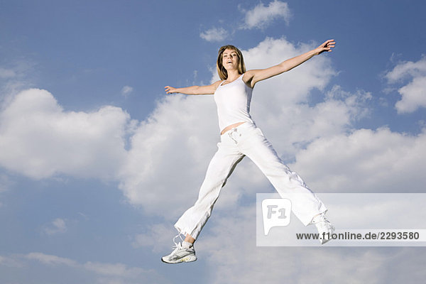 Junge Frau springt in der Luft  Arme ausgestreckt  lächelnd