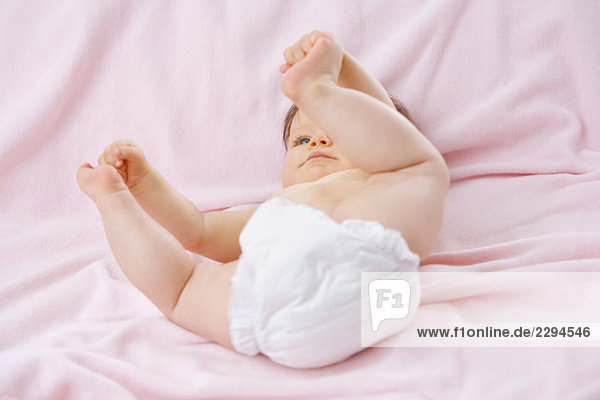 Kleines Mädchen (6-9 Monate) auf dem Bett liegend  Zehen berührend