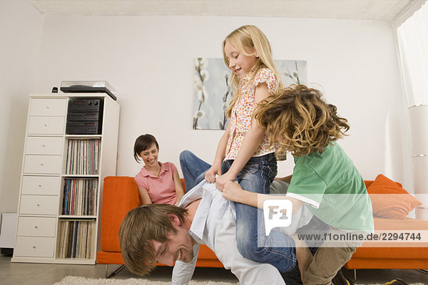 Boy (6-7) and girl (8-9) on father's back in living room