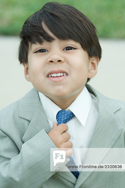 Young boy dressed in suit  adjusting tie  looking at camera