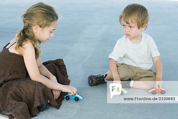 Bruder und Schwester sitzen auf dem Boden  spielen mit Spielzeugautos  Junge runzelt die Stirn.