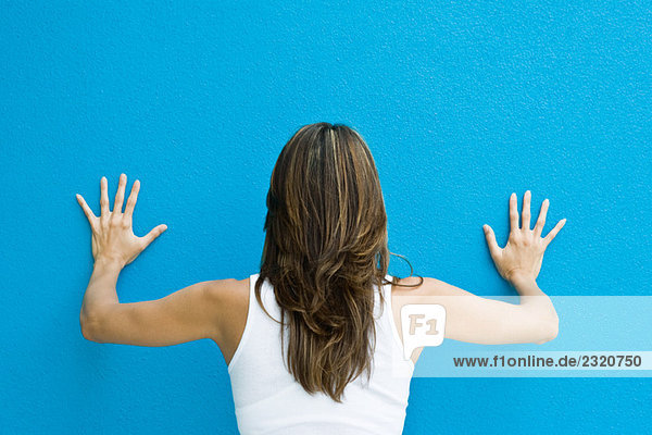Woman standing with hands against blue wall  rear view