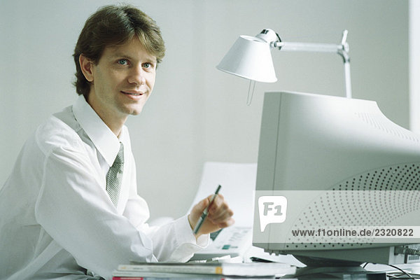 Geschäftsmann am Schreibtisch vor dem Computer sitzend  lächelnd  aufblickend