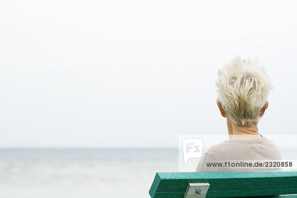 Seniorin am Meer sitzend  Rückansicht