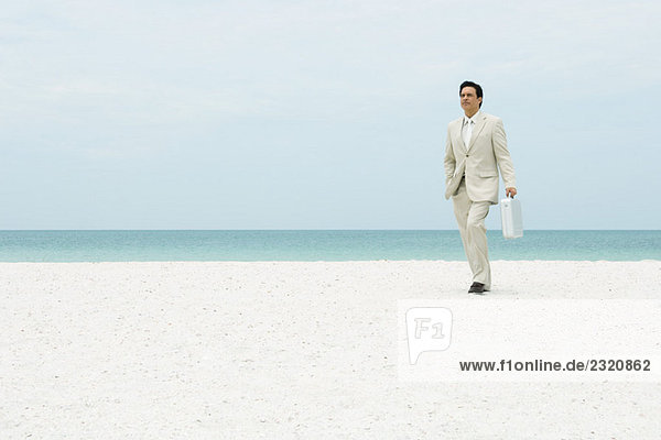 Geschäftsmann  der über den Strand läuft und eine Aktentasche trägt.