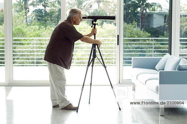 Man standing in living room  looking through telescope  side view