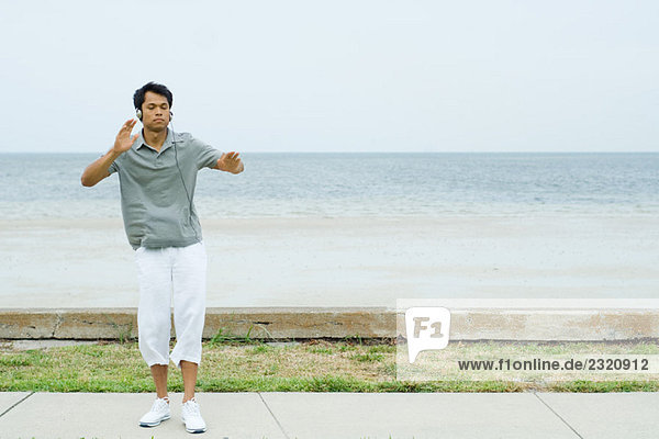 Mann steht mit ausgestreckten Armen am Strand  hört Kopfhörer  Augen zu.