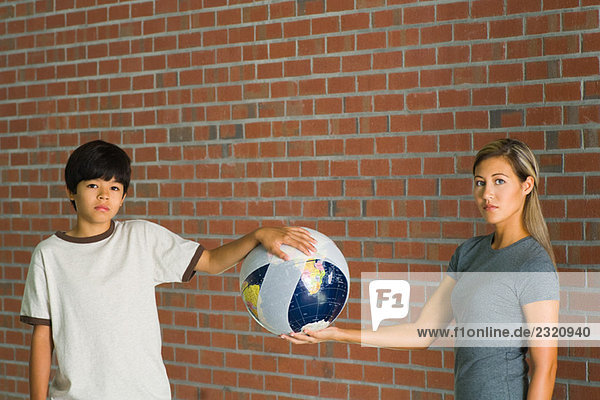 Frau und Junge halten den Globus in Bandagen gewickelt  beide schauen in die Kamera.