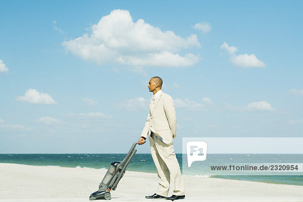 Man in suit standing on beach  using vacuum cleaner  side view