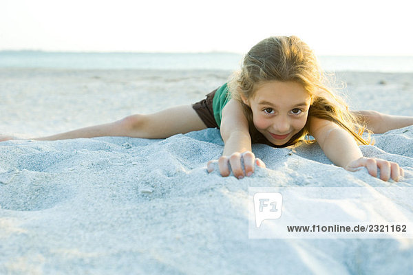 Kleines Mädchen im Sand am Strand liegend  lächelnd vor der Kamera