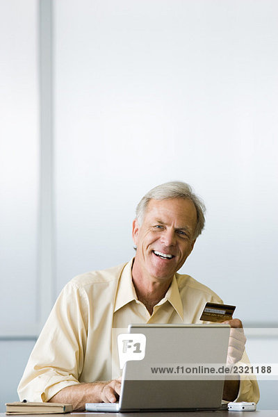 Man using laptop computer  holding credit card  smiling at camera