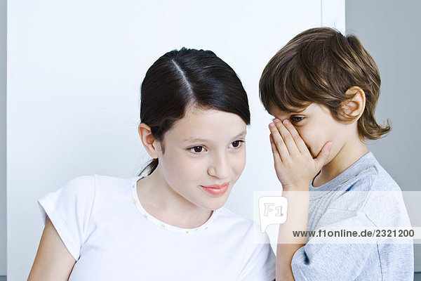 Kleiner Junge flüstert Schwester ins Ohr  Mädchen lächelt