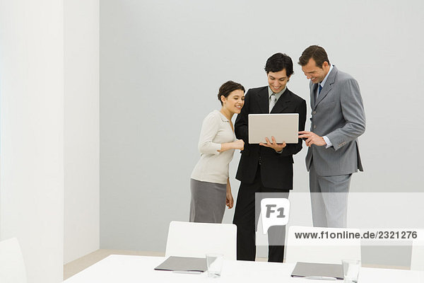 Drei Geschäftspartner stehen im Konferenzraum und schauen gemeinsam auf den Laptop.