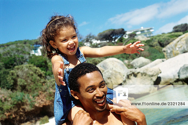 Father carrying daughter on shoulders at the beach  both smiling  close-up