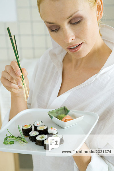 Frau hält Maki-Sushi und Essstäbchen und schaut nach unten.
