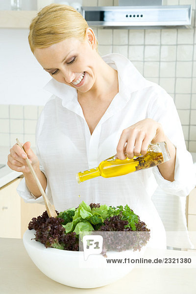 Frau in der Küche  Olivenöl auf großen Salat gießen