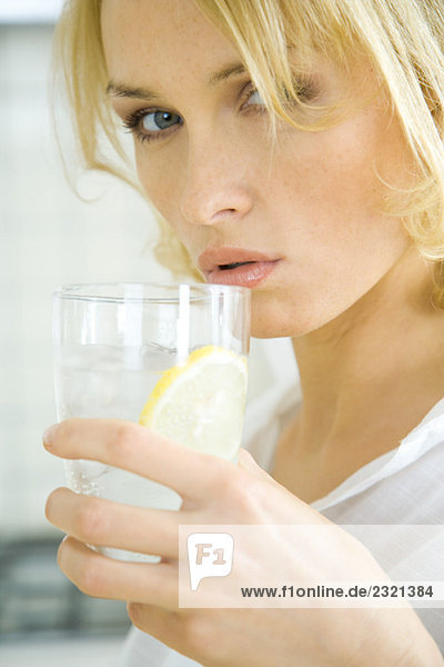 Frau trinkt Wasser mit Zitronenscheibe  Blick in die Kamera  Nahaufnahme