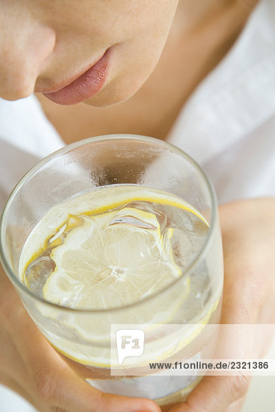 Frau hält Wasserglas mit schwimmender Zitronenscheibe  Nahaufnahme  beschnitten