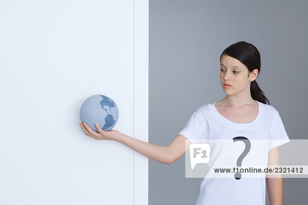 Mädchen im T-Shirt mit Fragezeichen bedruckt  Blick auf Globus