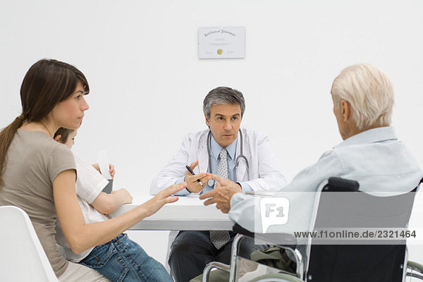 Doctor sitting at desk  having discussion with senior patient and his family