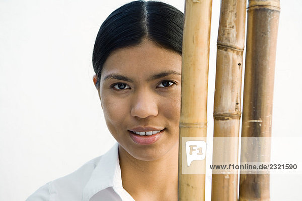 Woman standing behind bamboo stacks  looking at camera  portrait