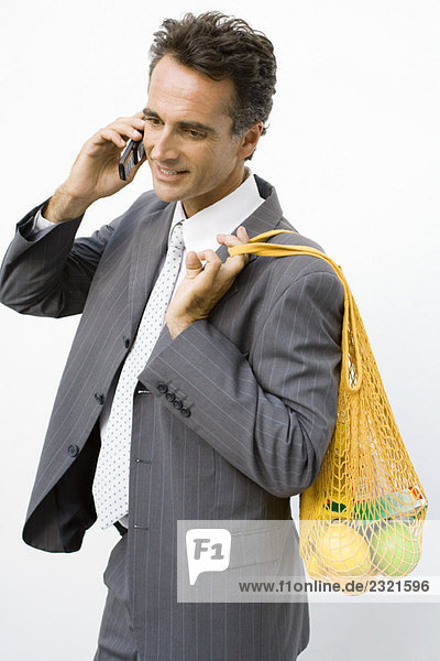 Geschäftsmann hält wiederverwendbare Einkaufstasche über die Schulter  per Handy