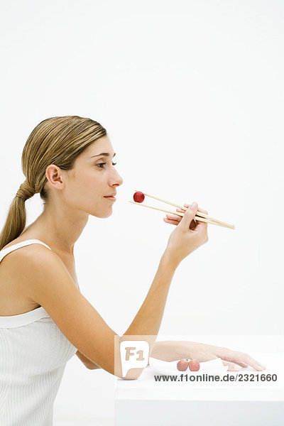 Junge Frau sitzend  Traube mit Stäbchen essen  Seitenansicht