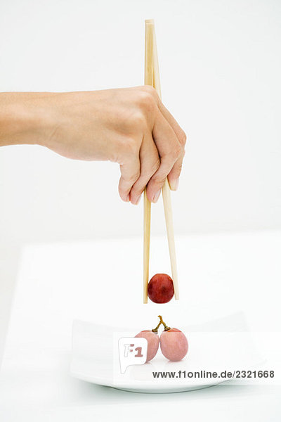 Frau nimmt rote Trauben mit Stäbchen auf  Blick von Hand abgeschnitten