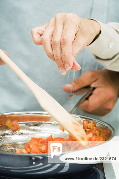 Gemeinsames Kochen  Frau streut Salz in die Pfanne  Ausschnittansicht