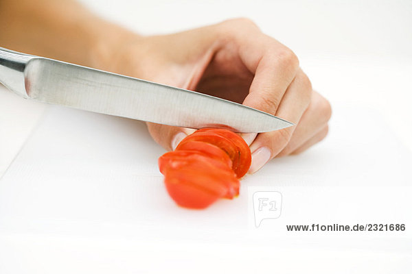 Frau schneidet Tomate mit Messer  abgeschnittene Ansicht der Hand