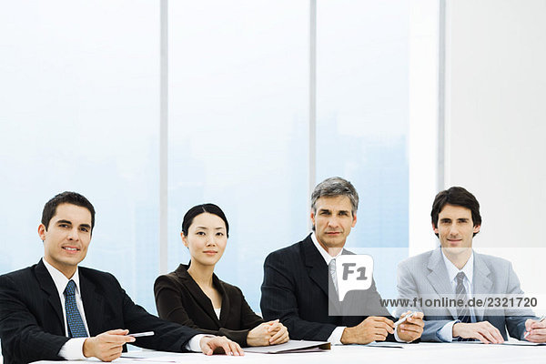 Group of business associates seated at table  looking at camera