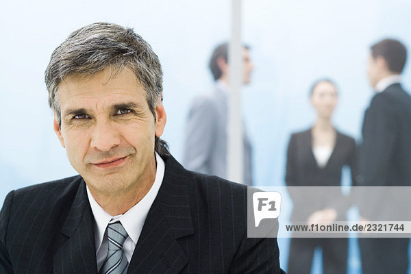 Businessman smiling at camera  colleagues in background