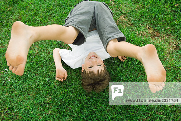 Junge auf dem Boden liegend  mit Beinen in der Luft  lächelnd in die Kamera  hohe Blickwinkel